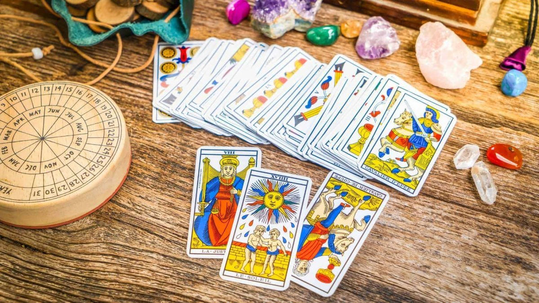 A deck of Tarot cards spread across a wooden table, surrounded by crystals and a divination tool.