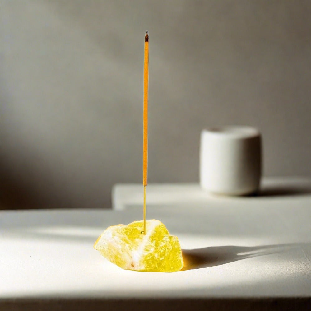 A yellow Citrine rough crystal incense holder holding a lit incense stick.