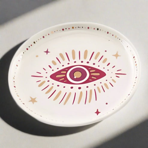 A top view of the white trinket dish that features a red and gold Evil Eye design.