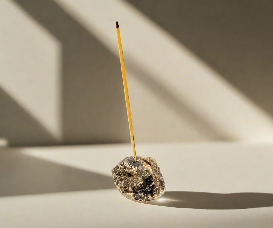 A rough Labradorite crystal incense holder holding a lit incense stick.