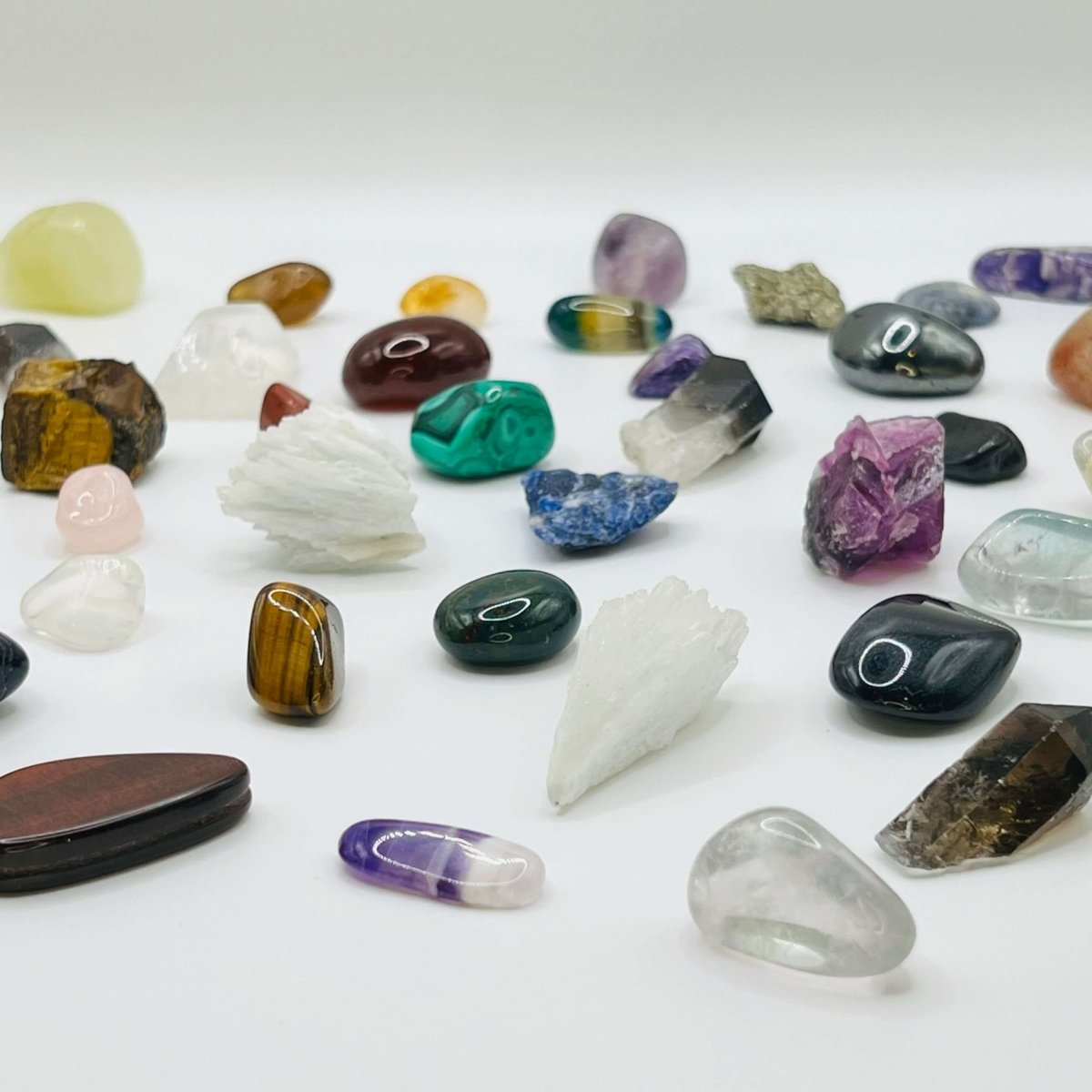 A selection of rough and tumblestone crystals equal distance from one another on a white background.