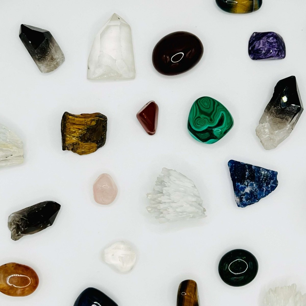 A selection of rough and tumblestone crystals equal distance from one another on a white background.