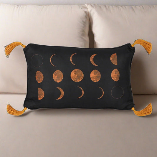 A black rectangle cushion that features different moon phases in gold. It also has gold corner tassels.