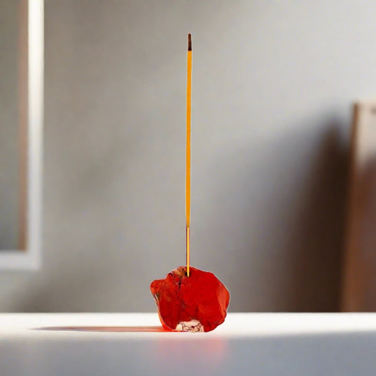 A rough Red Jasper crystal incense holder holding a lit incense stick.