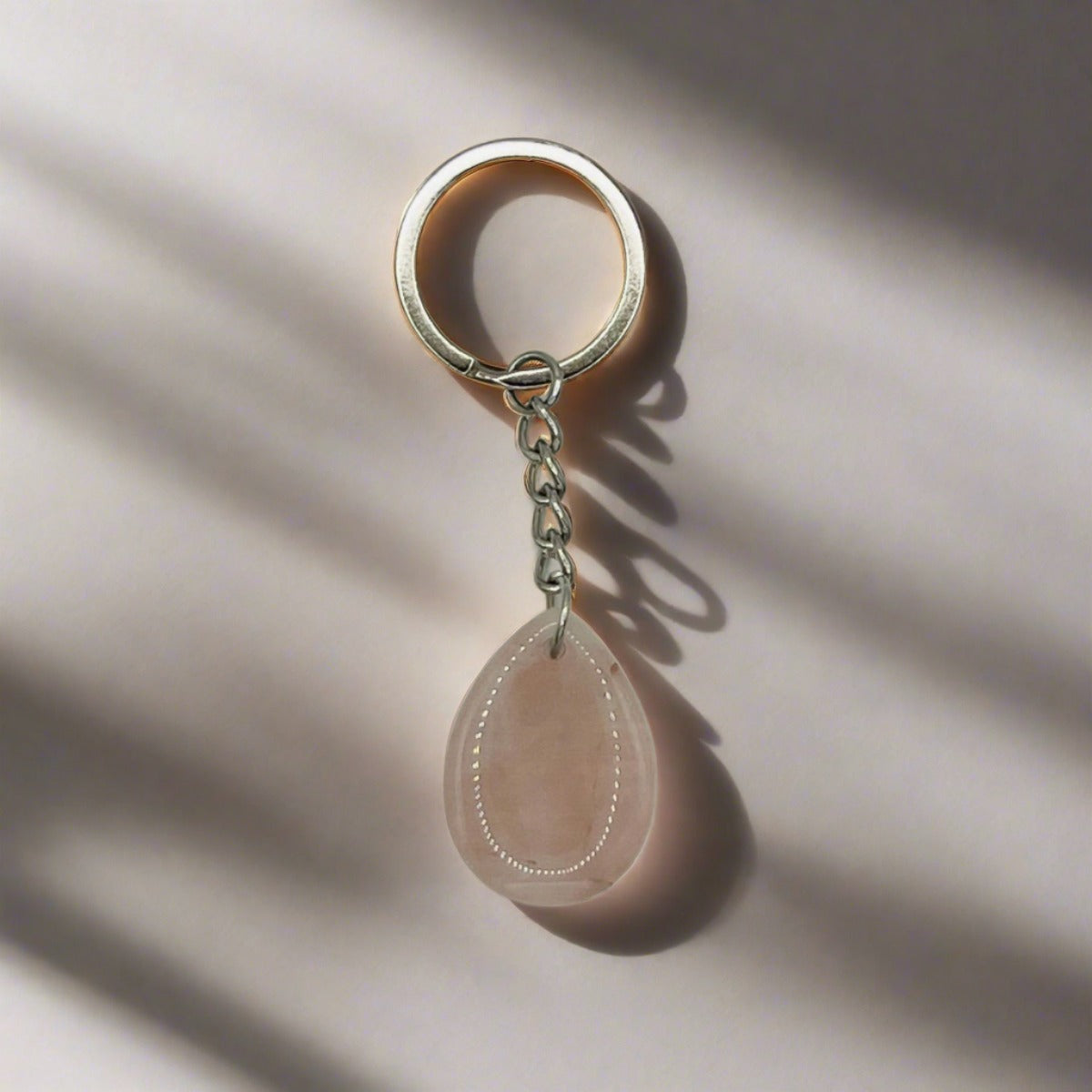 A teardrop-shaped Rose Quartz tumbled crystal stone on a silver keychain.