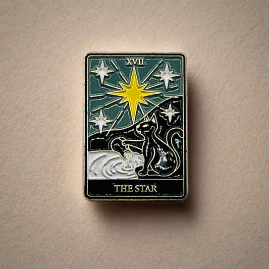 An enamelled The Star Tarot Card pin badge featuring a black cat and a yellow star.