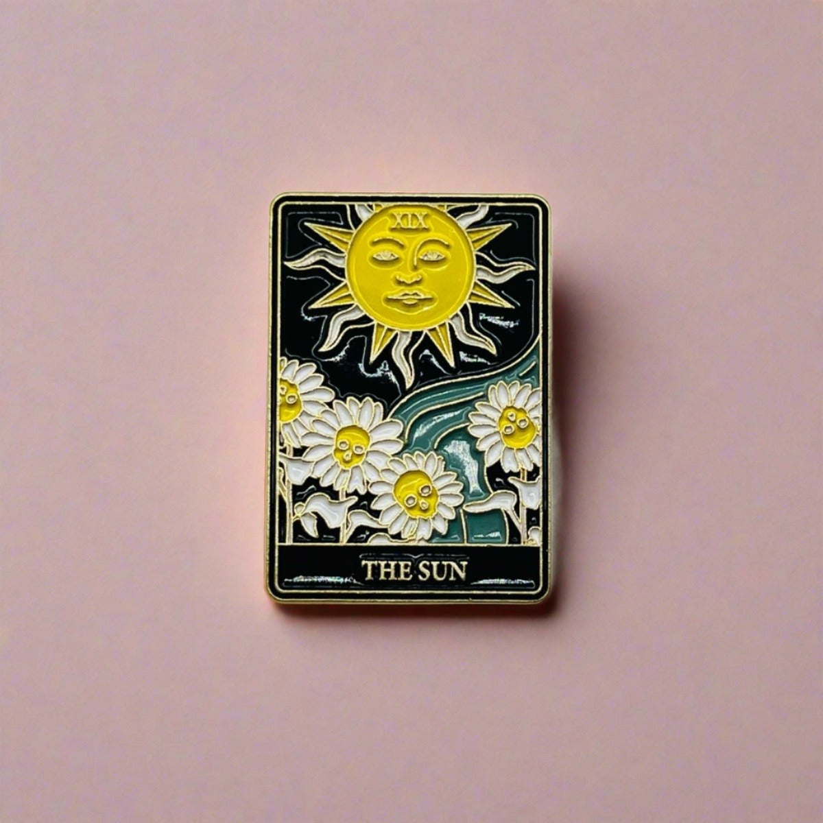 A black, white and yellow enamelled The Sun Tarot Card pin badge featuring a sun over looking daisy flowers.